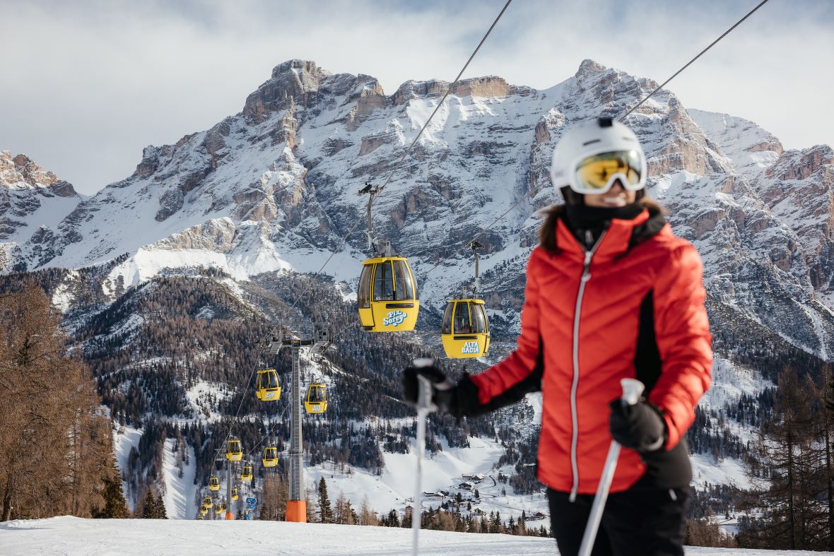 Skiers standing in front of Piz Sorega gondola lift above San Cassiano with Dolomites in the background