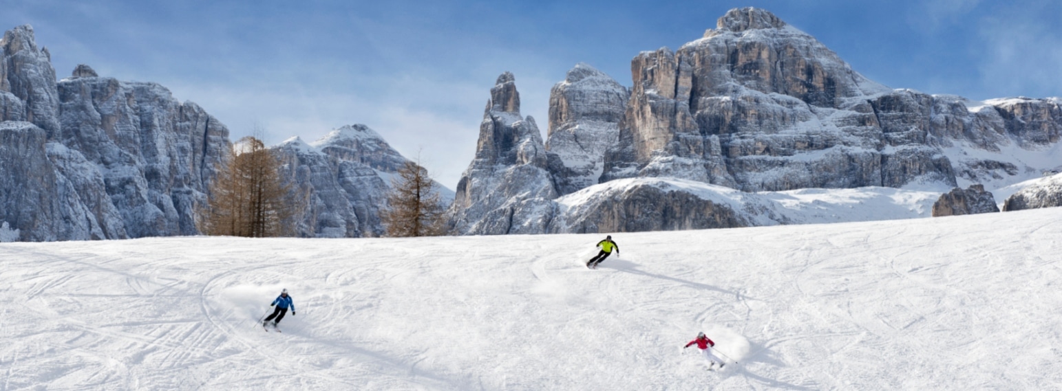 Three skiers descending a piste in Alta Badia surrounded by the Italian Dolomites